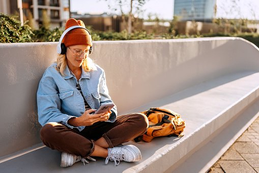 Young hipster woman text messaging while sitting on a bench outdoors