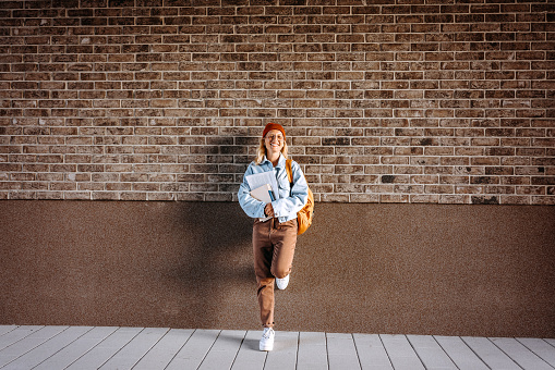 Portrait of smiling young hipster woman standing in front of brick wall on campus