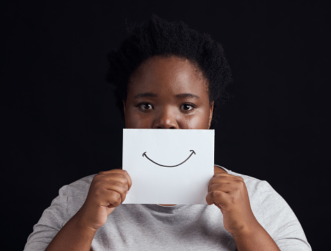 Paper smile, portrait and a black woman on a studio background for mental health, problem or fear. Advertising psychology, poster and the face of an African patient or girl with bipolar or sad