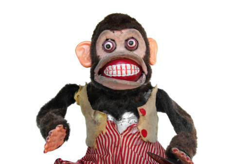 Damaged mechanical chimp with ripped vest, uneven eyes, missing cymbal