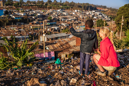 African little girl standing with young caucasian woman and pointing at houses in Kibera slum, Kenya, East Africa. Kibera is the largest slum in Nairobi, the largest urban slum in Africa, and the third largest in the world