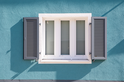 White window in a house with open plastic shutters.