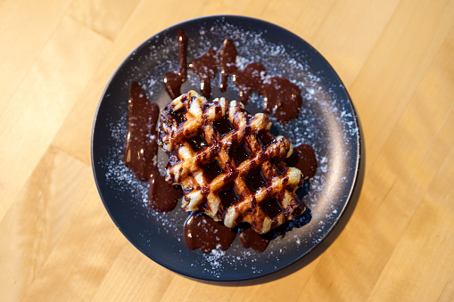 A Belgian waffle topped with chocolate spread and dusted with icing sugar.