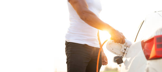 istock World Environment Day. save world save life concept. Hispanic driver electric car holding electrical plug connector to charge the batteries hybrid car at home or charging station. 1600902129