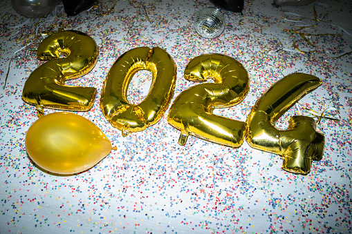 A party mess of left over gold foil 2024 new year balloons and confetti on the floor