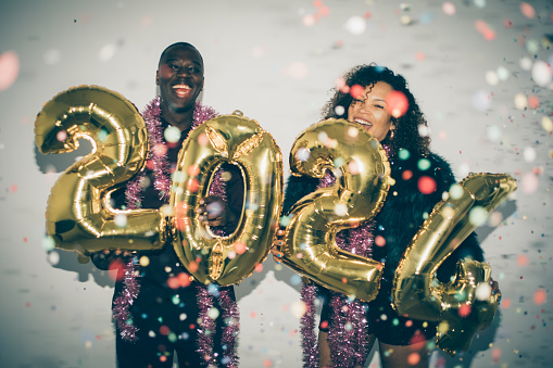 A festive couple are holding gold inflated numbered balloons for a Happy New Year 2024 on white background