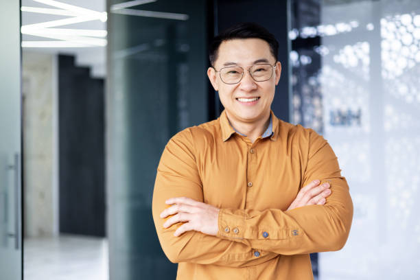 Portrait of successful asian businessman, man inside office wearing shirt and glasses smiling and looking at camera, investor broker with crossed arms near window Portrait of successful asian businessman, man inside office wearing shirt and glasses smiling and looking at camera, investor broker with crossed arms near window. taiwan people stock pictures, royalty-free photos & images