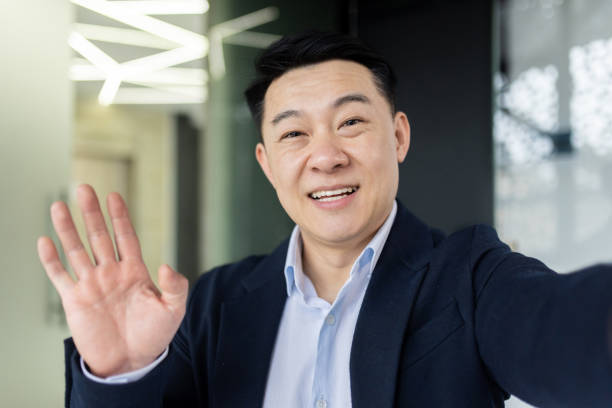 istock Asian man talking on video call using online communication app on phone, businessman in office taking selfie and smiling at camera, man greeting waving hand while talking with friends 1600937877