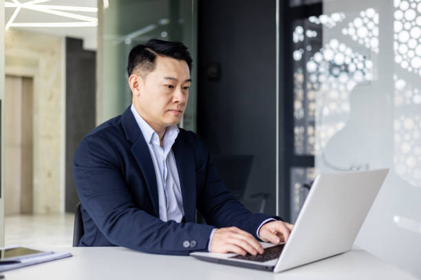 istock Serious and thoughtful businessman working inside office sitting at table using laptop at work, mature asian boss thinking and typing on keyboard 1600940196