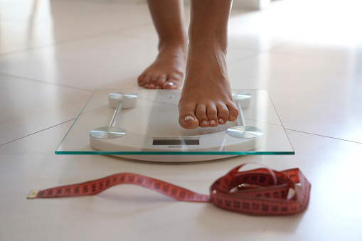Female feet stepping on weight scale. Healthy lifestyle, food and sport concept.