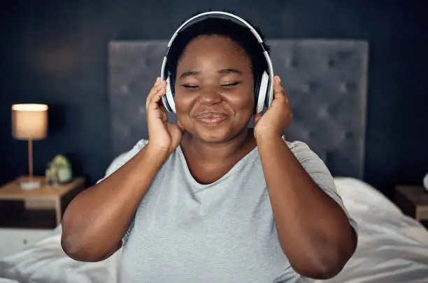 Photo of Crying, smile and black woman with headphones for music, sound or audio. Tears, radio and plus size African person listening, hearing and streaming podcast for peace or relax in home bedroom at night