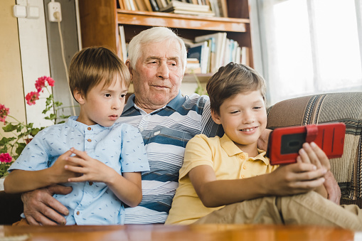 Grandfather and grandsons are sitting on the couch and watching a funny video on their smartphone