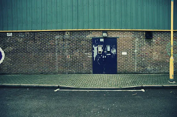 Soccer goal roughly drawn on a wall outside an industrial building. Sign to one side reads - 'Private Property . No Ball Games'. Cross processed.