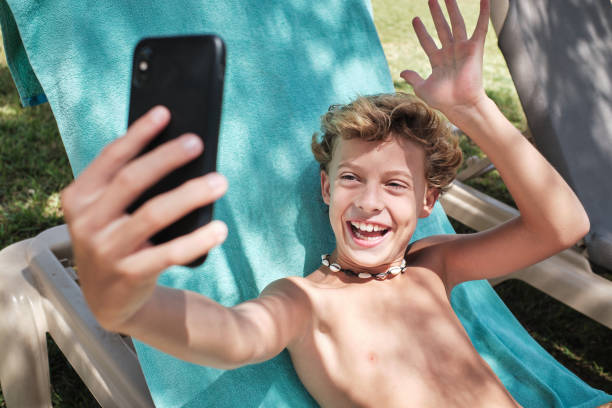 istock Cheerful boy sitting and taking selfie on poolside 1601021998