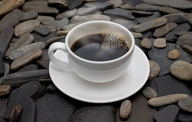 white cup of coffee against black stones stock photo