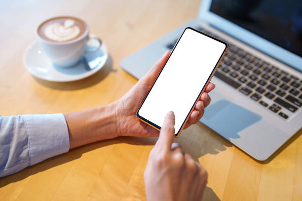 istock A mockup image featuring a woman holding a smartphone with a blank white screen. The desk includes a laptop computer and a cup of coffee as the background 1601029615