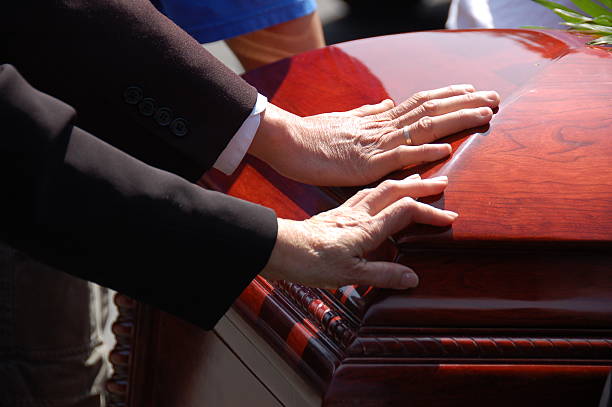 Husband and Wife Funeral Farewell 2 hands touching a closed wooden casket.  Farewell to a loved one. coffin photos stock pictures, royalty-free photos & images