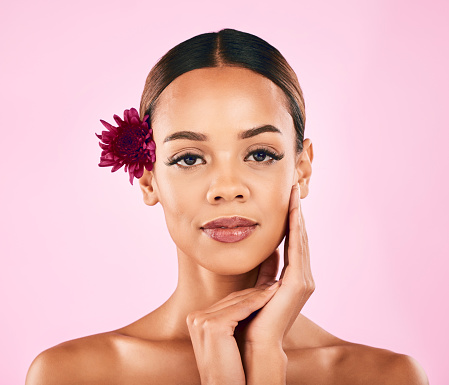 Skincare, cosmetics and portrait of woman with flower, makeup and wellness glow on pink background. Natural beauty, dermatology and model with luxury facial care and healthy spa aesthetic in studio.