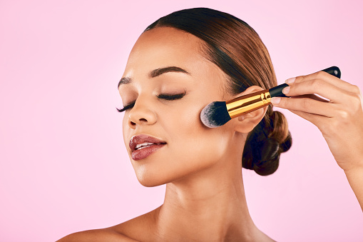 Calm woman, face and brushes for makeup, beauty or cosmetics against a pink studio background. Female person or model with cosmetic tools, brush or equipment for grooming or applying facial treatment