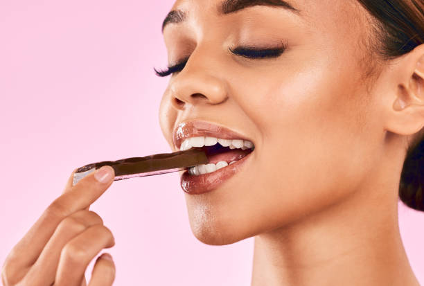 Happy woman, face and eating sweet chocolate, cocoa or delicious dessert against a pink studio background. Closeup of calm female mouth, lips or teeth biting and enjoying tasty sugar food or candy Happy woman, face and eating sweet chocolate, cocoa or delicious dessert against a pink studio background. Closeup of calm female mouth, lips or teeth biting and enjoying tasty sugar food or candy candy in mouth stock pictures, royalty-free photos & images