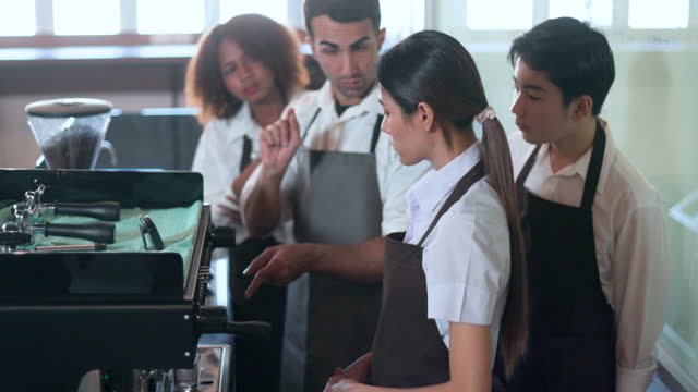 Group of diverse students learning to use coffee machine from expert barista in classroom