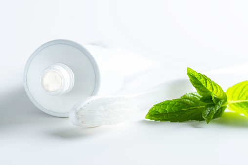 White toothpaste tube , toothbrush and green mint leaf on white background.
