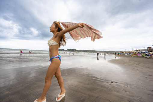 Woman in bikini visiting summer beach, holding blanket