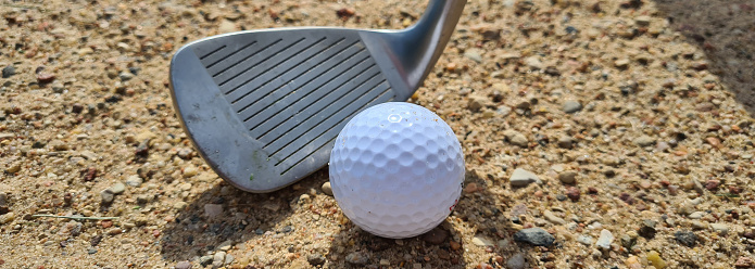 Golf ball trapped with wedge of sand about to hit golf ball. Sand golf
