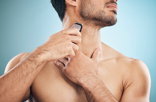 Hands, shaving and electric razor with a man in studio on a blue background for personal hygiene or grooming. Beauty, wellness and cosmetics with a young male in the bathroom for hair removal