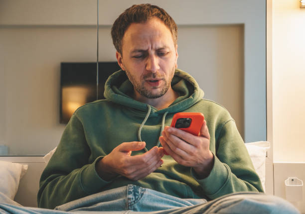 Mature middle age man using phone, reading internet news and typing message on sofa at home