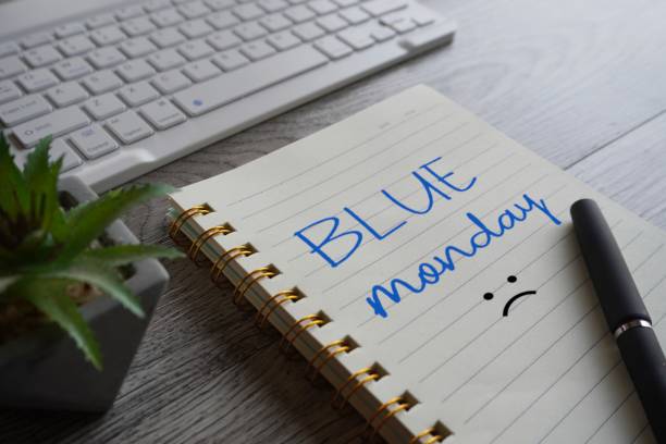Notebook with text BLUE MONDAY, pen and laptop on table