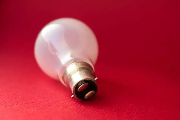A traditional bayonet tungsten bulb laying on a red background