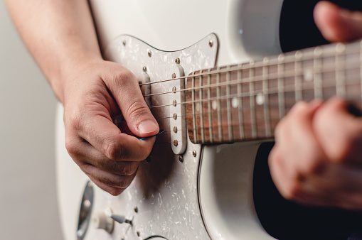 close up unrecognizable caucasian man playing electric guitar with plectrum, focus on right hand, copy space.