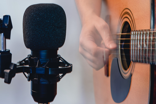 closeup condenser microphone with blurred man playing acoustic guitar with plectrum in the background with copy space, recording music in studio with professional microphone.