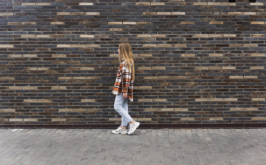 young woman walks down the street against a brick wall