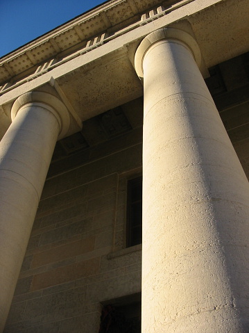 Vertical image looking up on the columns of a state house or court house. Sky slightly in background.