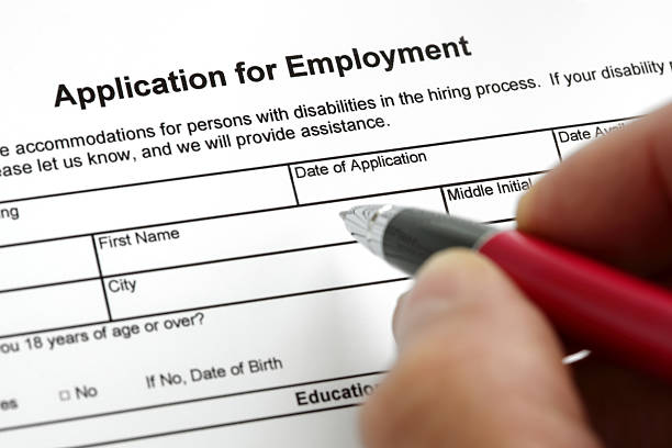 A hand with a pen filling out an application for employment Completing a job application form with focus on heading application form stock pictures, royalty-free photos & images