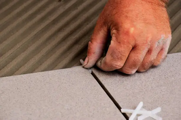 male worker's hands close-up view. laying ceramic floor tiles in grooved troweled cement grout on concrete base slab. work in progress. construction work process. home renovation concept.