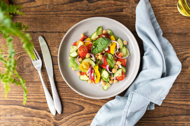 istock Vegetarian vegetable salad with chickpeas, tomatoes, red onions, cucumbers and lettuce. Vegetarian food rich in protein and fiber. Vegetable salad on wooden table top view 1601171340
