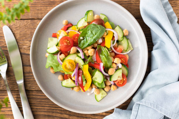 istock Vegetarian vegetable salad with chickpeas, tomatoes, red onions, cucumbers and lettuce. Vegetarian food rich in protein and fiber. Vegetable salad on wooden table top view 1601172906
