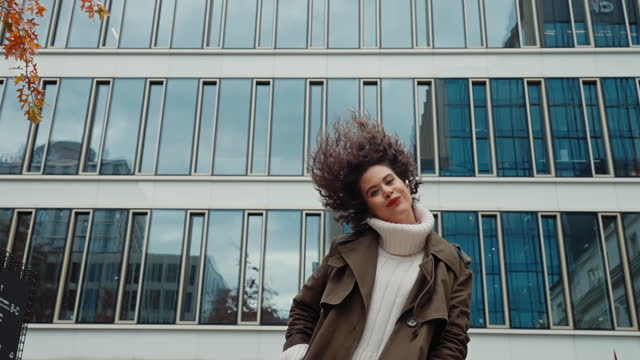 Cheerful female with curly hair having fun run and jump turning to camera autumn city street