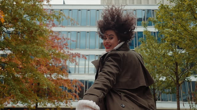Cheerful female with curly hair having fun run and jump turning to camera autumn city street