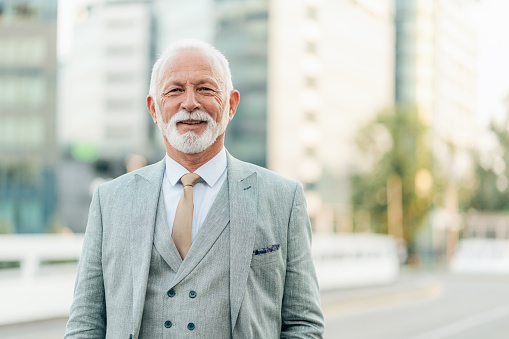 Portrait of elegant senior businessman looking at camera and smiling. Mature business entrepreneur with formal businesswear standing outdoor in the city street