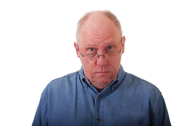 istock Older Balding Man in Blue Shirt Looking Over Glasses 160120611