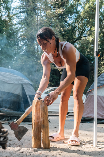 A female camper holding an axe and a small log of wood at a campsite in Big Sur, California.