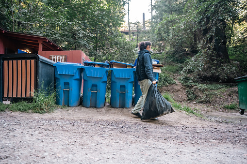 A male camper about to dispose off a trash bag into a recycling dumpster while camping in Big Sur, California.