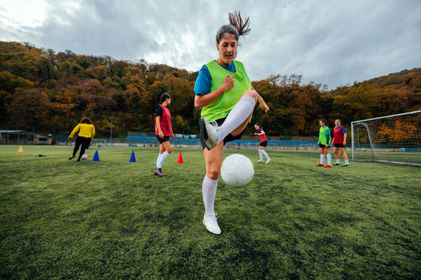 Teenage girl practicing soccer, kicking the ball towards the goal with the goalkeeper ready to defend