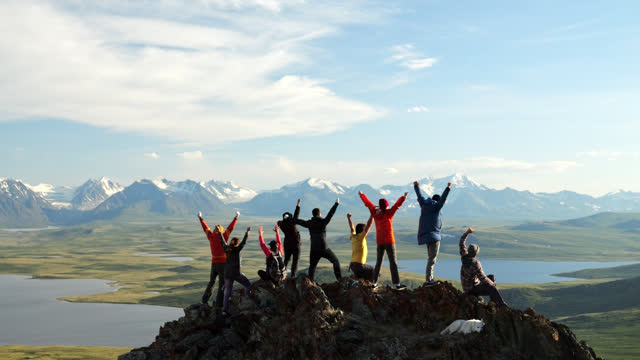 Travel group together raise arms and joy achievement on mountain top back view