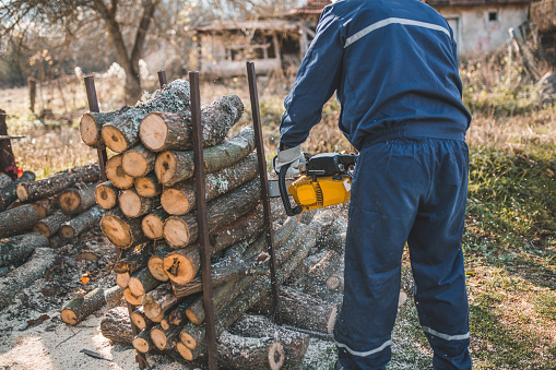 Handsome middle-aged man chopping wood with axe at backyard of country house. Man with chopper standing near woodpile.