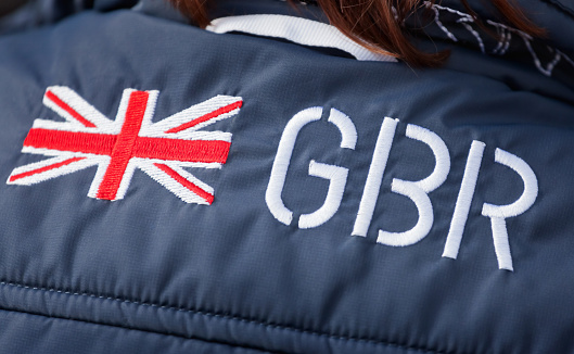 Lady wearing a jacket with an embroidered Union Jack flag badge motif and the GBR insignia. Patriotic support for the sports Great Britain, or GBR, Team, which includes representatives from England, Wales, Scotland and Northern Ireland united under a single patriotic flag the Union Jack. This effectively constitutes a United Kingdom National Team.